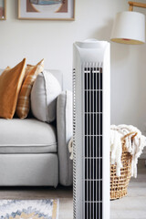 White tower fan against the background of a sofa and a basket with blankets in a modern light...