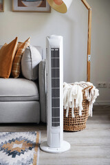 White tower fan against the background of a sofa and a basket with blankets in a modern light...