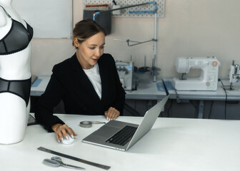Tailor working on a laptop in a sewing workshop with mannequin 