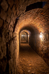 Obraz premium A long, underground corridor in a historic fortress, with brick-arched ceilings lit by a series of warm lights. Picture taken on a holiday trip to Kłodzko Fortress, Poland with my Sony a7III