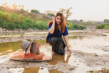 A woman poses for the camera, brushing her hair back as she kneels in the river at sunset. A...