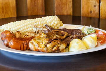 Ecuadorian roast served on a white plate, with a mix of meats like chicken, sausage, and beef,...