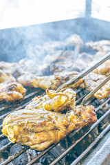 Using grill tongs, flip a grilled chicken over hot coals. Succulent meat browns in the smoke and open fire. A traditional dish, perfect for family gatherings and weekend occasions.