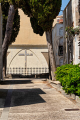 A stone cross at the end of a path in a classic Mediterranean cemetery with cypress trees. The path...