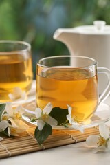 Tasty jasmine tea in cups, teapot and flowers at white wooden table, closeup