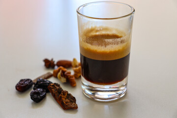  Glass of strong espresso served with assorted dried fruits on a white table