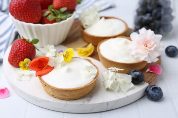 Delicious dessert. Tartlets with cream, berries and flowers on white tiled table, closeup