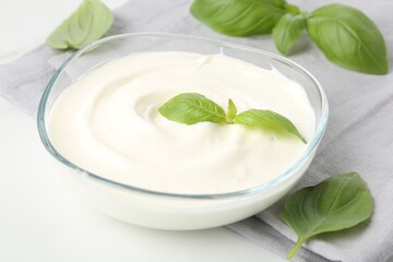 Tasty yoghurt with basil in bowl on white table, closeup