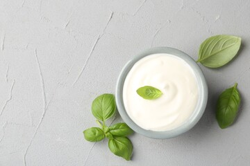 Tasty yoghurt with basil in bowl on light grey table, flat lay. Space for text