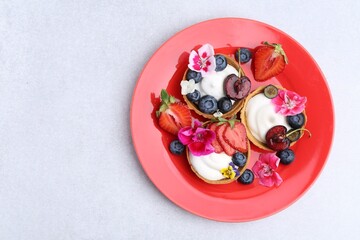 Sweet tartlets with berries and flowers on grey table, top view with space for text. Delicious...