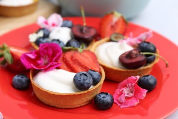 Sweet tartlets with berries and flowers on light table, closeup. Delicious dessert