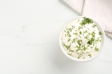 Delicious yogurt in bowl and dill on white marble table, top view. Space for text