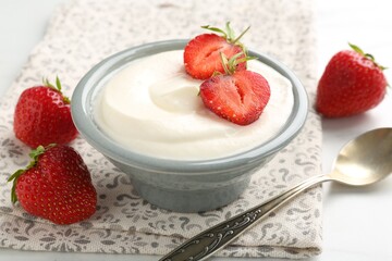 Delicious yogurt in bowl, strawberries and spoon on table, closeup