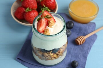 Tasty yogurt with granola, berries and honey on light blue wooden table, closeup