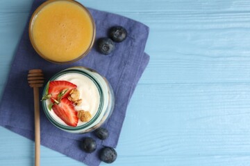 Tasty yogurt with granola, berries and honey on light blue wooden table, flat lay. Space for text