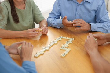 Friends playing dominoes at wooden table against light background, closeup