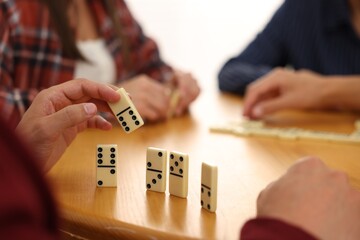 Friends playing dominoes at wooden table against light background, closeup