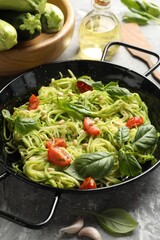 Tasty zucchini noodles with tomatoes, pine nuts, basil and ingredients on grey table, closeup