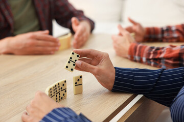 Friends playing dominoes at light wooden table, closeup
