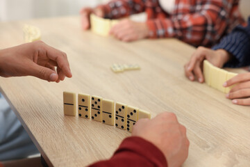 Friends playing dominoes at light wooden table, closeup