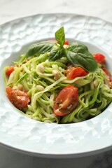 Tasty zucchini noodles with tomatoes, pine nuts and basil on white table, closeup