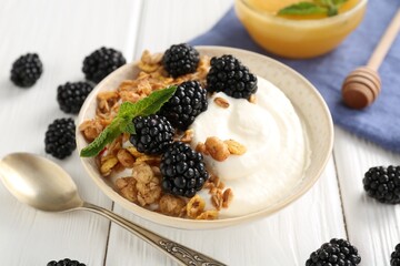 Tasty yogurt with granola, honey and blackberries in bowl on white wooden table, closeup