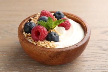 Tasty yogurt with granola and berries in bowl on wooden table, closeup