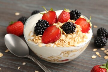 Tasty yogurt with granola and berries in bowl on wooden table, closeup