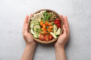 Healthy vegetarian food. Woman with delicious Buddha bowl at light grey table, top view