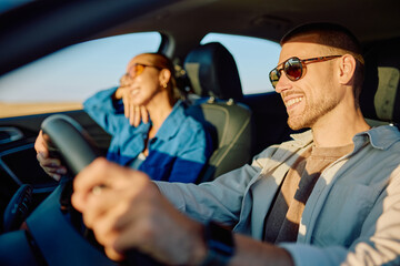 Young man and girlfriend driving through scenic landscapes during a road trip, basking in the warm...