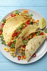 Tasty vegetarian tacos with chickpeas, corn and quinoa served on light blue wooden table, top view