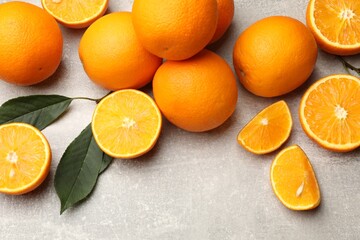 Fresh ripe oranges and green leaves on grey table, flat lay
