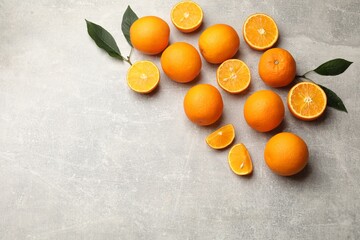Fresh ripe oranges and green leaves on grey table, flat lay. Space for text