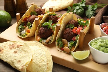 Tasty vegetarian tacos with falafel served with salsa and guacamole on wooden table, closeup