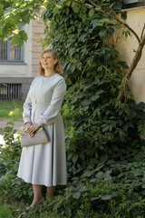Young woman with blond hair in retro blue dress walking in summer park.