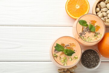 Superfood. Tasty smoothie with chia seeds, mint, pistachio and oranges on white wooden table, flat lay. Space for text