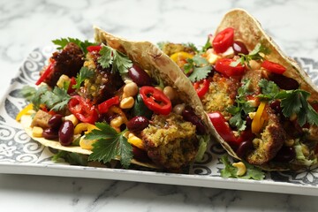 Tasty vegetarian tacos with falafel, tofu, beans and vegetables on white marble table, closeup