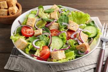 Delicious salad with croutons and vegetables served on wooden table, closeup