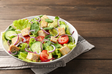 Delicious salad with croutons and vegetables on wooden table, closeup. Space for text