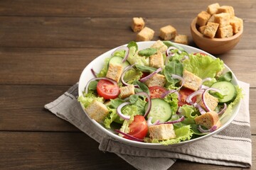 Delicious salad with croutons and vegetables on wooden table, closeup. Space for text