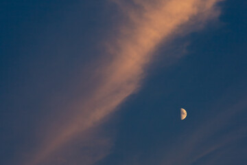 Abstract of quarter moon in dark blue sky with dramatic diagonal high orange cloud 