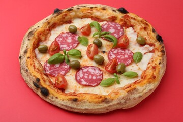 Delicious pizza with salami, olives, tomatoes and basil on red table, closeup