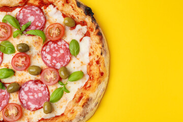 Delicious pizza with salami, olives, tomatoes and basil on yellow table, top view. Space for text