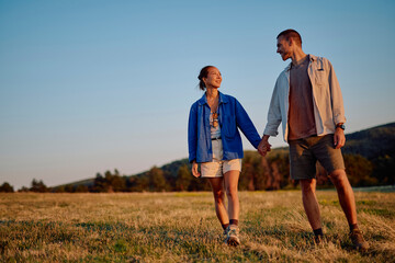Interracial couple enjoying a romantic walk in nature, holding hands and smiling at each other...