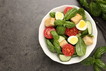 Tasty salad with croutons, tomatoes, cucumbers and basil on black table, flat lay. Space for text