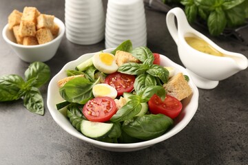 Tasty salad with croutons, tomatoes, cucumbers and basil on black table, closeup
