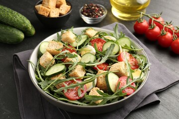 Tasty salad with croutons, cucumbers, tomatoes and arugula on black table, closeup