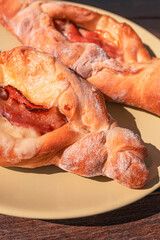 Close-up of two traditional Greek peinirli on a beige plate. These boat-shaped breads are filled with melted cheese and cured meat, with golden-brown crusts.