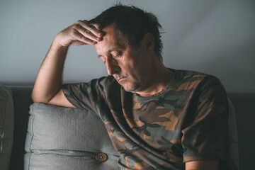 Portrait of pensive middle-aged man rethinking in dark room at night