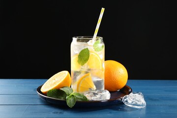 Sparkling water with orange, ice and mint in glass on blue wooden table, closeup